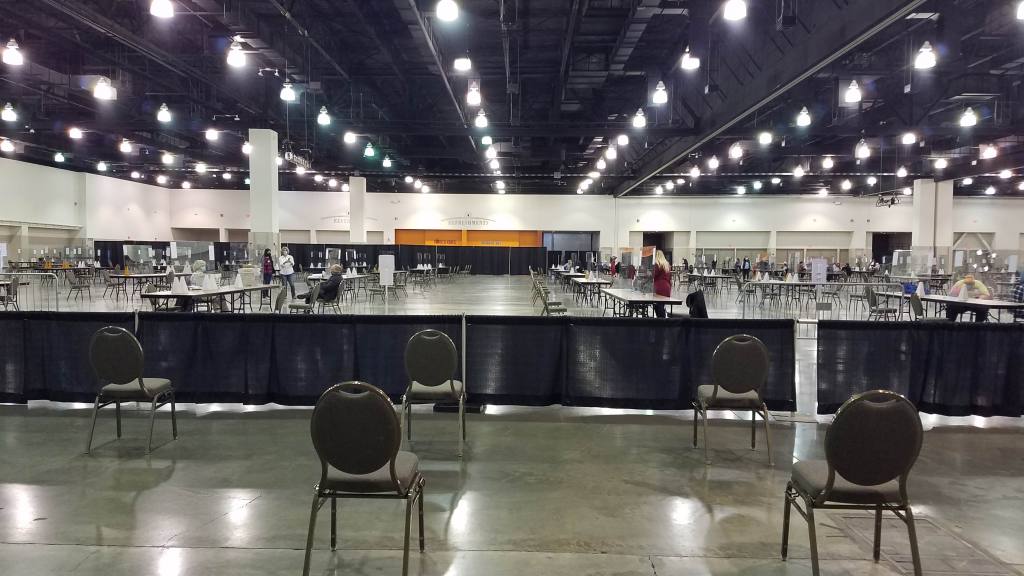 A large, empty room with tables set up and a fabric barrier between some chairs and the rest of the room where the tables are situated. 